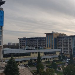Chmielewski-Nieruchomości - Widok z góry na kompleks apartamentowo-hotelowy z wyraźnym podziałem na sekcje o różnej architekturze i kolorystyce, otoczony zielenią drzew i krzewów, z parkingiem widocznym w tle, pod pochmurnym...