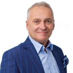 Portret uśmiechniętego mężczyzny w niebieskim garniturze w kratę i błękitnej koszuli na białym tle, z poszetką w kwiatowy wzór.