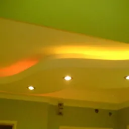 Sufit podwieszany z płyty karton gips z dekoracyjnym oświetleniem LED i trzema punktowymi lampami halogenowymi, pomalowany na żółto-pomarańczowy odcień, widok z dołu.