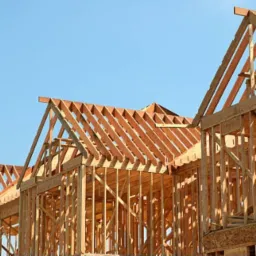 Surowe drewniane ramy kilku domów w trakcie budowy, widoczne na tle błękitnego nieba.