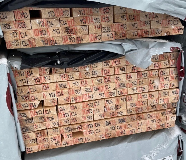 Stos tarcicy budowlanej C14 z czerwonymi oznaczeniami, zabezpieczony folią, widok z góry pod kątem.