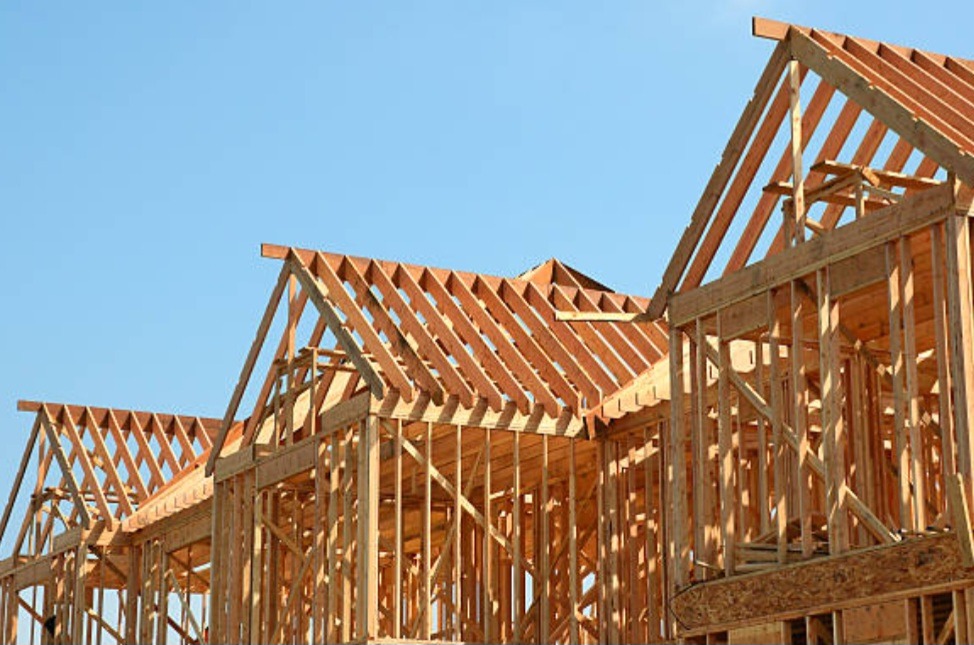 Surowe drewniane ramy kilku domów w trakcie budowy, widoczne na tle błękitnego nieba.