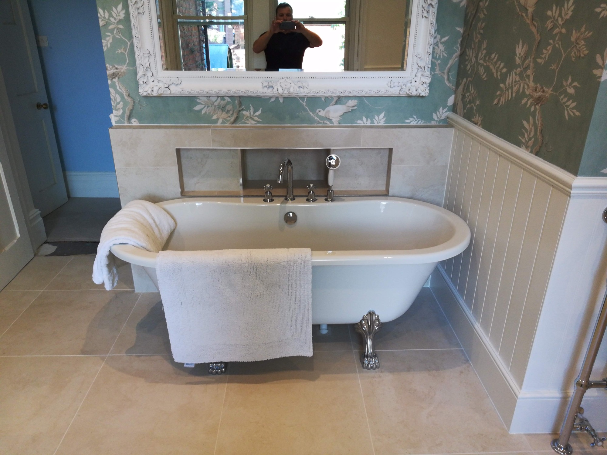 Wolnostojąca wanna na lwich łapach w wykończonej łazience, z baterią retro i ręcznikami, odbicie fotografa w ozdobnym lustrze.