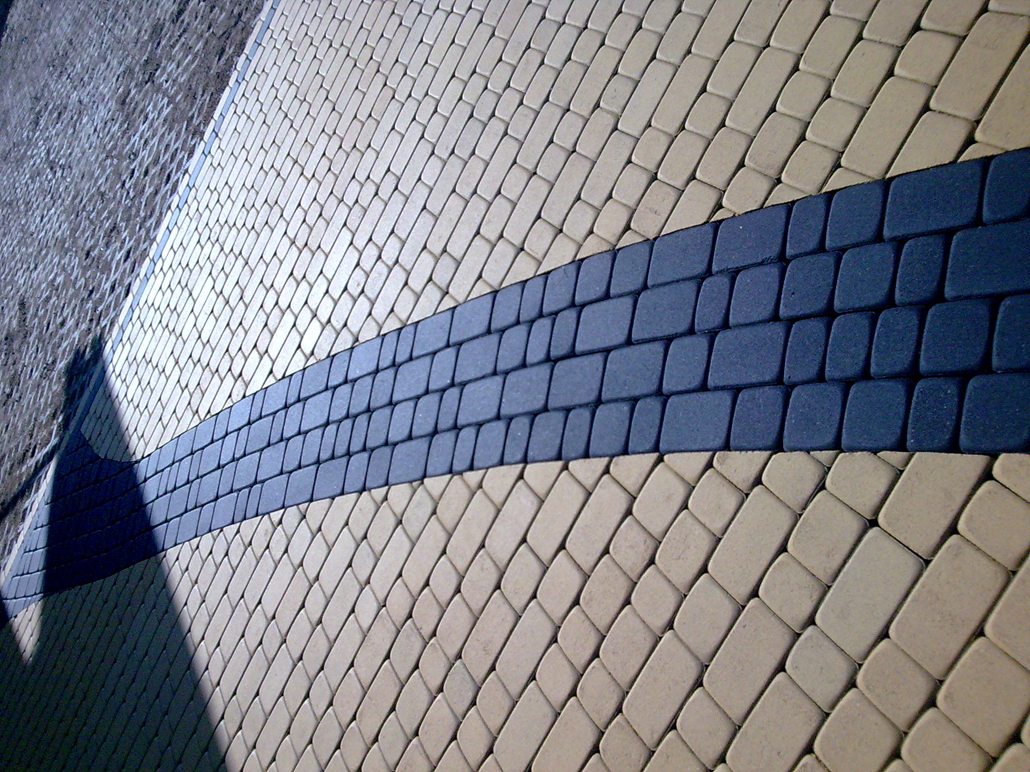 Ułożona nawierzchnia z kostki brukowej w beżowym i niebieskim kolorze, ułożona pod kątem, z widocznym cieniem po lewej stronie.