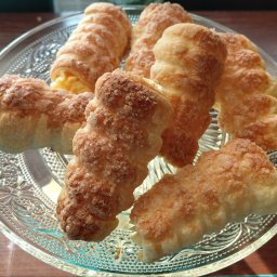 Przetwórnia Smaku Arleta Olbrych - Kremówki w kształcie rożków, posypane cukrem, ułożone na szklanym, zdobionym talerzu. Widoczne kremowe nadzienie. Słodki deser.