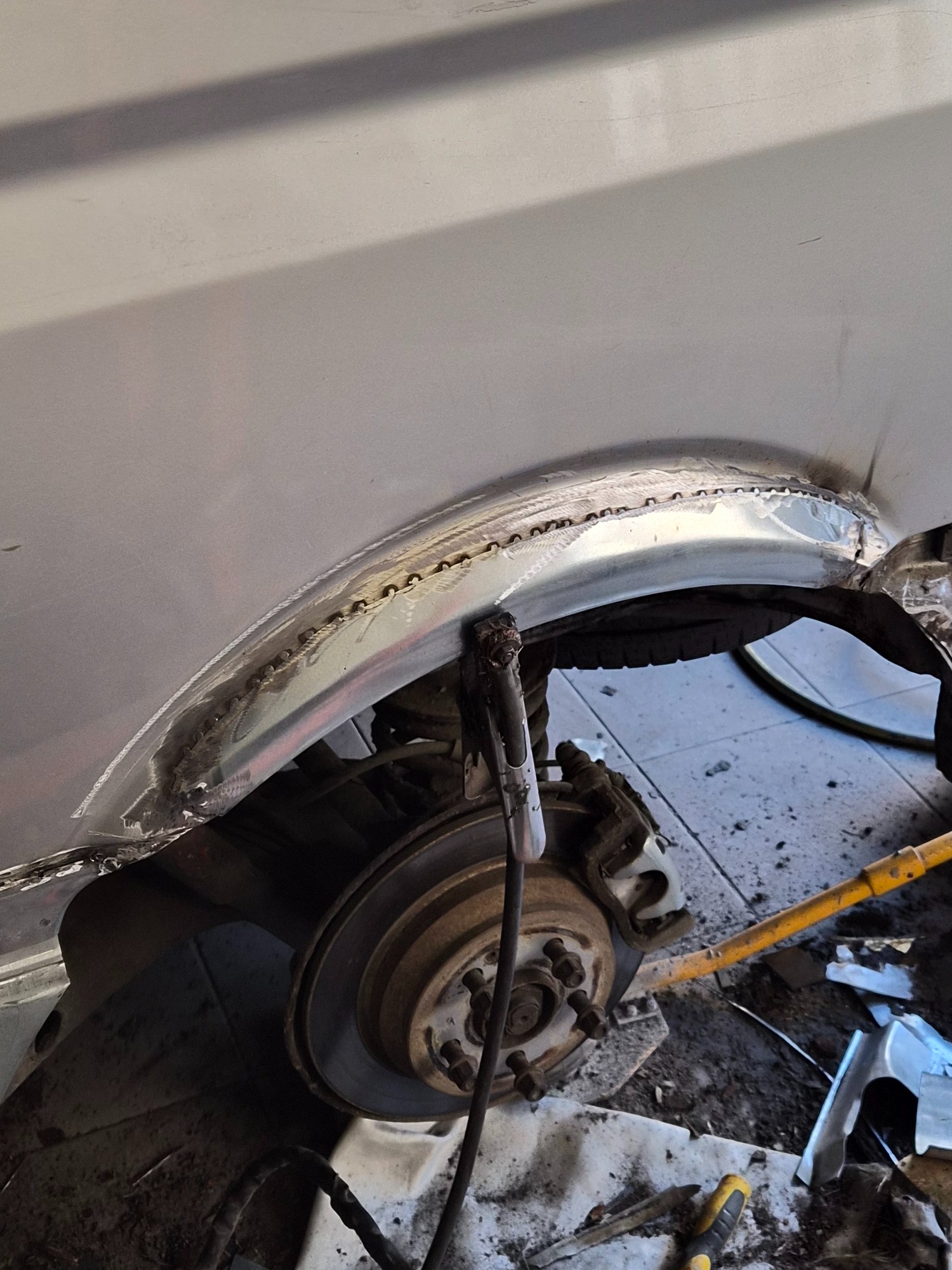 Spawanie nadkola samochodu. Widoczne łączenia blach i elementy zawieszenia. Detaliczny widok na proces naprawy karoserii w warsztacie.