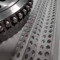 Metalowa tarcza z wypustkami oraz trzy białe, perforowane listwy z otworami ułożone na jasnym tle.