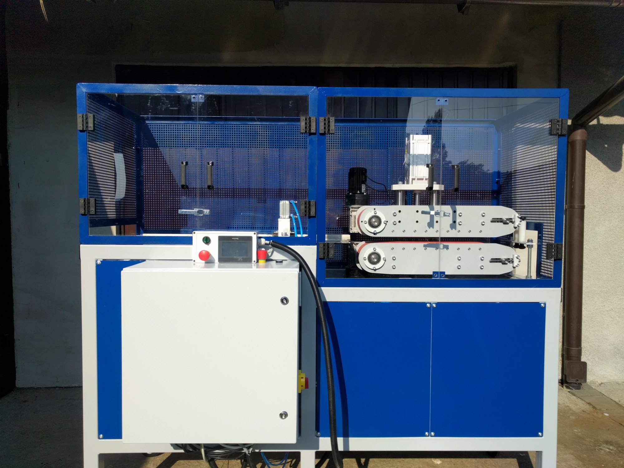 Automatyczna linia produkcyjna z osłoną bezpieczeństwa, panelem sterowania i elementami pneumatycznymi, widoczne napędy i rolki transportowe.