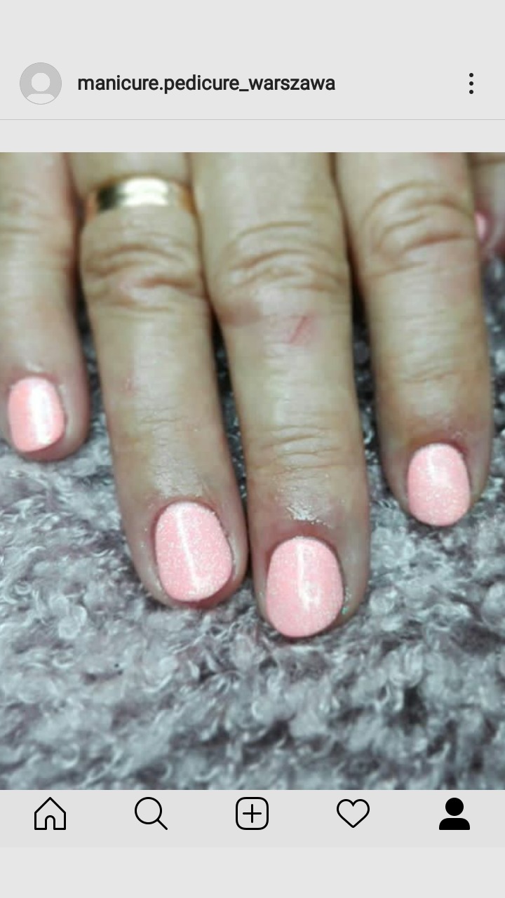 Dłoń z świeżo pomalowanymi, błyszczącymi paznokciami w odcieniu pastelowego różu, na tle miękkiego, szarego koca.