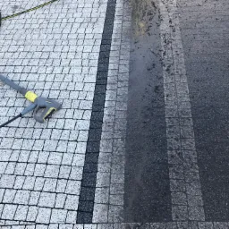 Czyszczenie kostki brukowej myjką ciśnieniową, widoczny efekt przed i po czyszczeniu. Po lewej stronie kostka wyczyszczona, po prawej brudna.