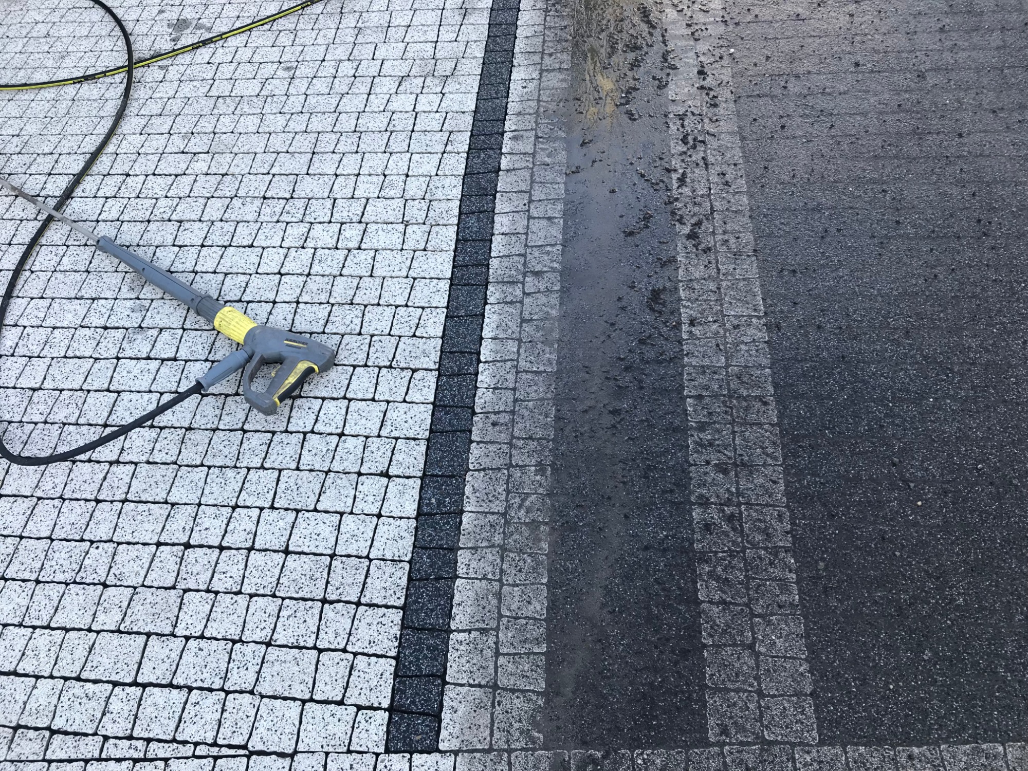 Czyszczenie kostki brukowej myjką ciśnieniową, widoczny efekt przed i po czyszczeniu. Po lewej stronie kostka wyczyszczona, po prawej brudna.