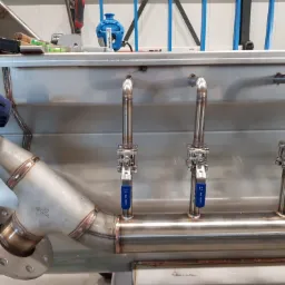 Spawane rury ze stali nierdzewnej z zaworami kulowymi, widoczne spoiny, narzędzia i poziomice w tle