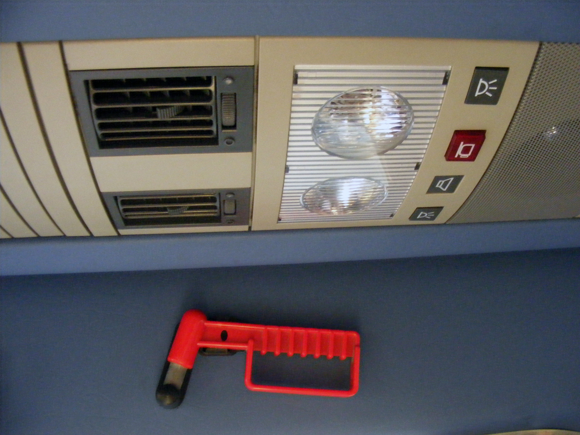 Wnętrze autobusu Mercedes-Benz Sprinter 413 CDI z widocznym panelem sterowania oświetleniem, nawiewami i głośnikiem oraz czerwonym młotkiem bezpieczeństwa do wybijania szyb.