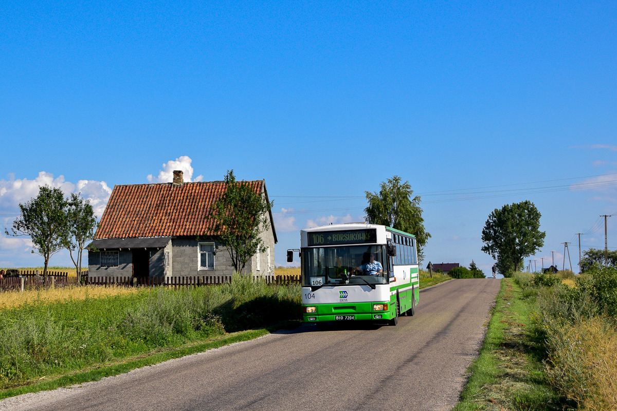 Jelcz 120MM/2 w zielono-białych barwach linii 106 wjeżdża na wzniesienie asfaltowej drogi, w tle niewielki dom z ceglanym dachem i błękitne niebo.