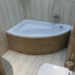 Narożna wanna obudowana mozaiką w beżowych odcieniach, dopasowana do płytek na ścianach i podłodze, widoczny fragment toalety i umywalki.