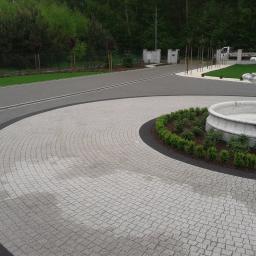 Lech-Bruk Lech Mędykowski - Podjazd wyłożony szarą kostką granitową w kształcie wachlarza, obrzeże z ciemnej kostki, w tle fontanna i zadbana zieleń.