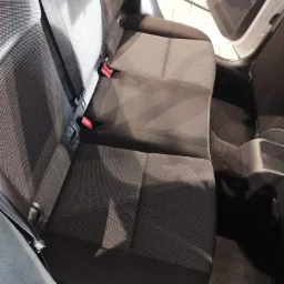 Wnętrze samochodu z widoczną tylną kanapą z szarej tapicerki materiałowej po praniu, z widocznymi zapięciami pasów bezpieczeństwa i fragmentem dywanika podłogowego.