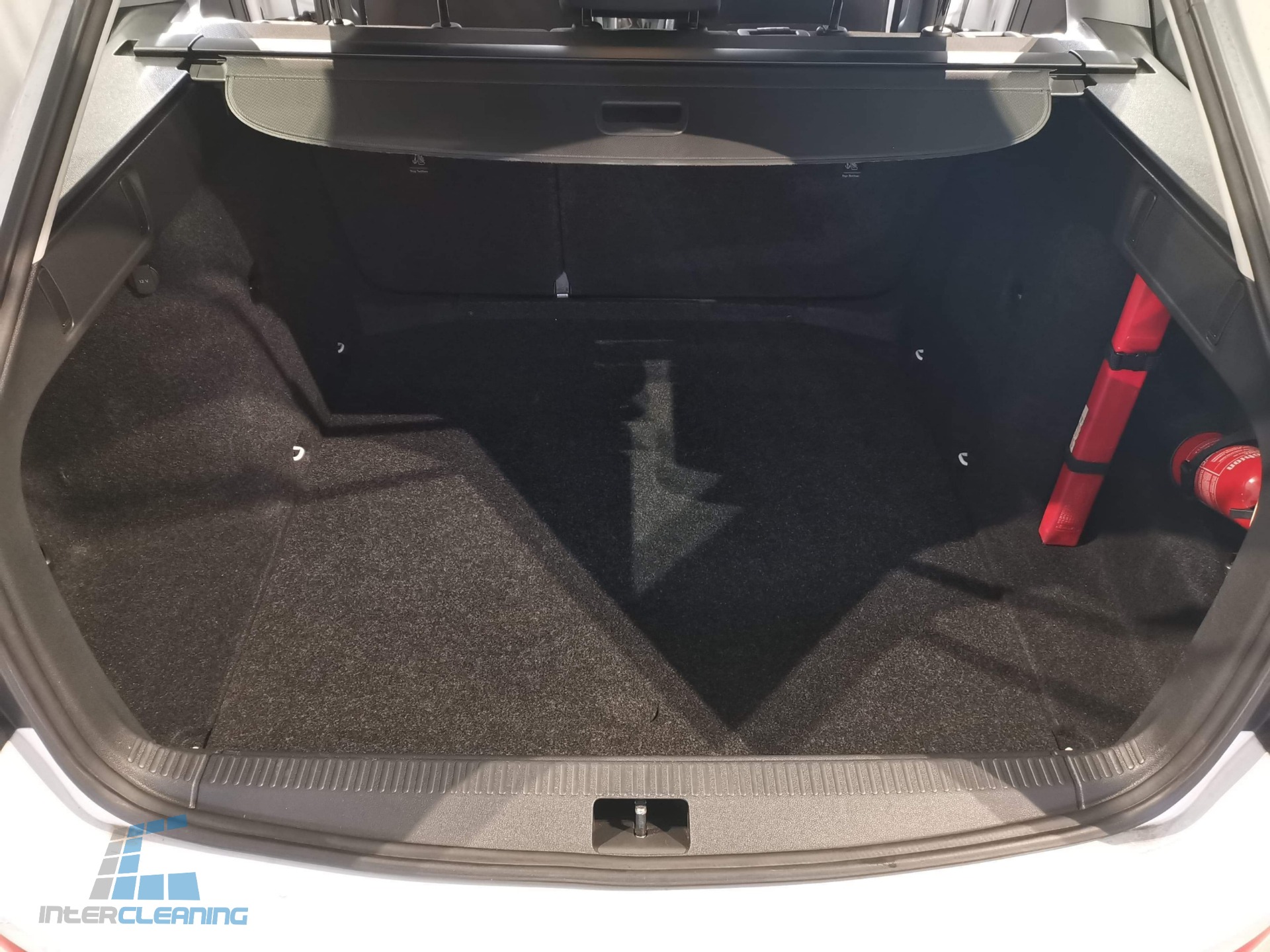 Czysty, pusty bagażnik samochodu z czarną wykładziną, widoczny trójkąt ostrzegawczy i gaśnica po prawej stronie.