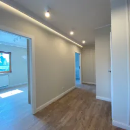 Jasne panele podłogowe w korytarzu w Trzebini, widok na pomalowane ściany w odcieniach beżu i oświetlenie sufitowe LED.