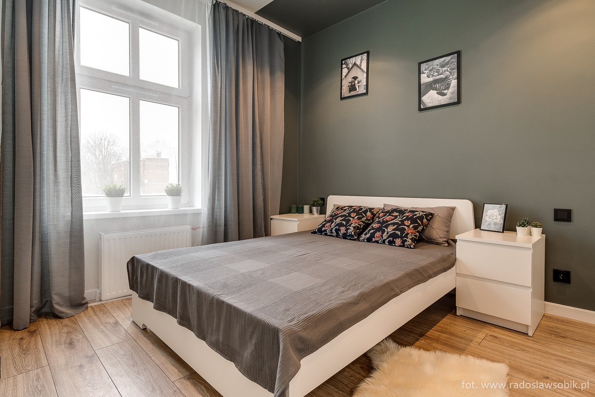 Sypialnia w odcieniach szarości i zieleni z drewnianą podłogą, białym łóżkiem i szafkami nocnymi, dekoracjami na ścianach i futrzanym dywanikiem.