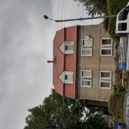 Dwupiętrowy budynek z nowym, czerwonym dachem z dachówki, widoczne okna dachowe, elewacja w trakcie prac, obok zaparkowany biały bus z rusztowaniem na pace.