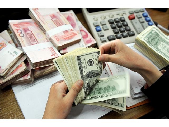 Dłonie liczą plik banknotów dolarowych na biurku z kalkulatorem i plikami chińskich juanów w tle.