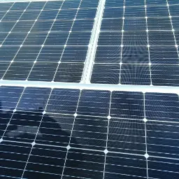 Niebiesko-czarne panele słoneczne z widocznym odbiciem sylwetki osoby na powierzchni, połączone srebrnymi wspornikami.