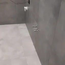 Szare płytki podłogowe i ścienne w nowoczesnej łazience z czarnym grzejnikiem drabinkowym i chromowanymi zaworami