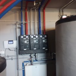 F.U.H Sanitec - Zestaw rozdzielaczy z manometrami, rury w izolacji czerwonej i niebieskiej, zbiornik akumulacyjny. Elementy instalacji grzewczej w kotłowni.