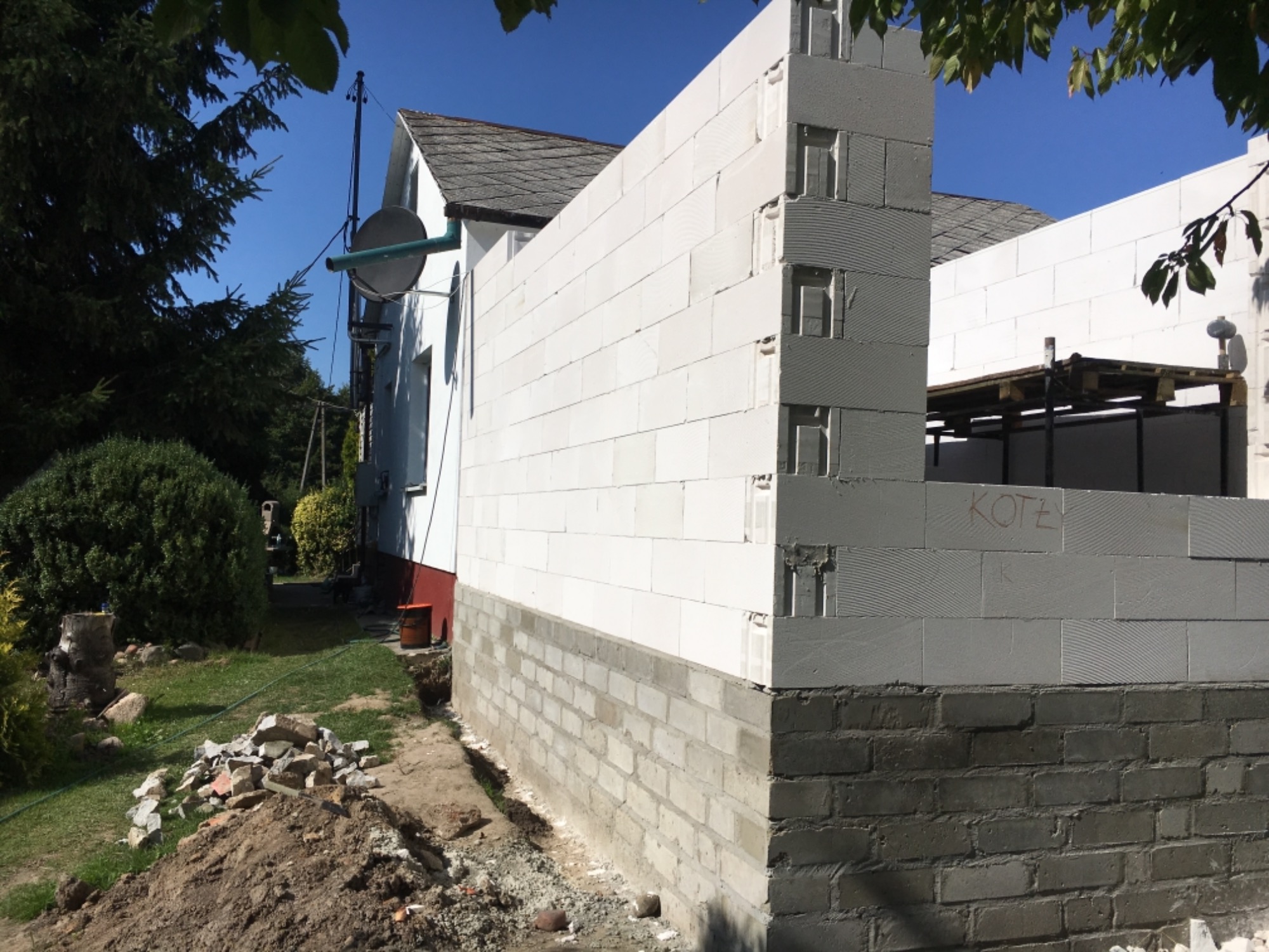 Wznoszenie ścian parteru z białych bloczków silikatowych na fundamencie z cegły; widoczny napis 'KOTŁY' na bloczkach i sterta gruzu obok.
