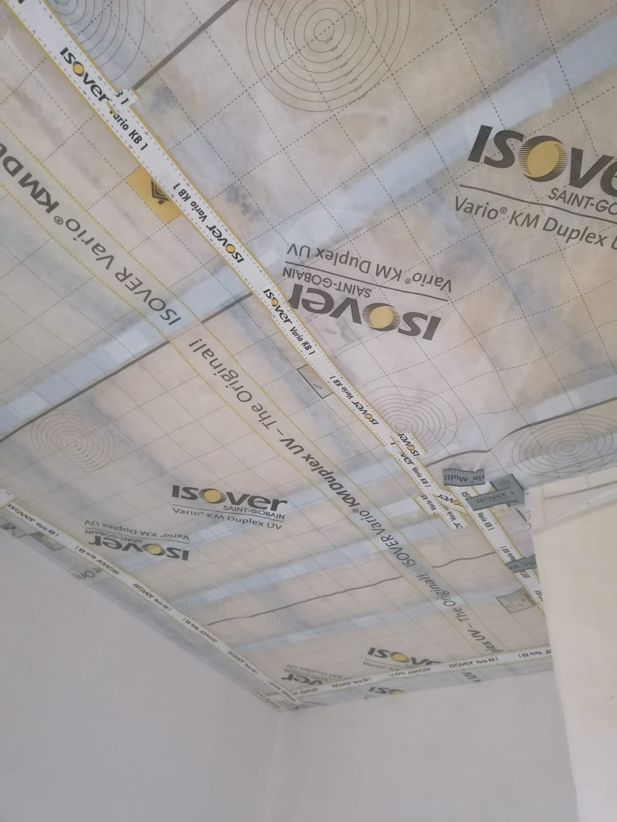 Montaż folii paroizolacyjnej Isover Vario KM Duplex UV na suficie, widoczne taśmy uszczelniające na zakładach folii.