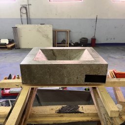 MAR-REM Usługi Remontowo Budowlane - Kamienna umywalka w kształcie prostopadłościanu, umieszczona na drewnianym stelażu w warsztacie. Widoczne narzędzia i materiały budowlane w tle. Surowy, industrialny charakter.
