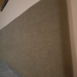 Pracownia Tapicerska Karol Krupa - Beżowy, tapicerowany zagłówek łóżka z tkaniny w prążki, widoczny fragment pikowanej narzuty na łóżko i fragment obrazu na ścianie.