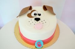 Tort w kształcie głowy psa z brązowymi uszami i łatką, różowym językiem i cyfrą '6' na niebieskim kółku u podstawy, na złotym podkładzie.