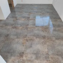 Ułożone płytki podłogowe w odcieniach szarości i beżu z delikatnym wzorem, widoczne białe ściany w surowym stanie.