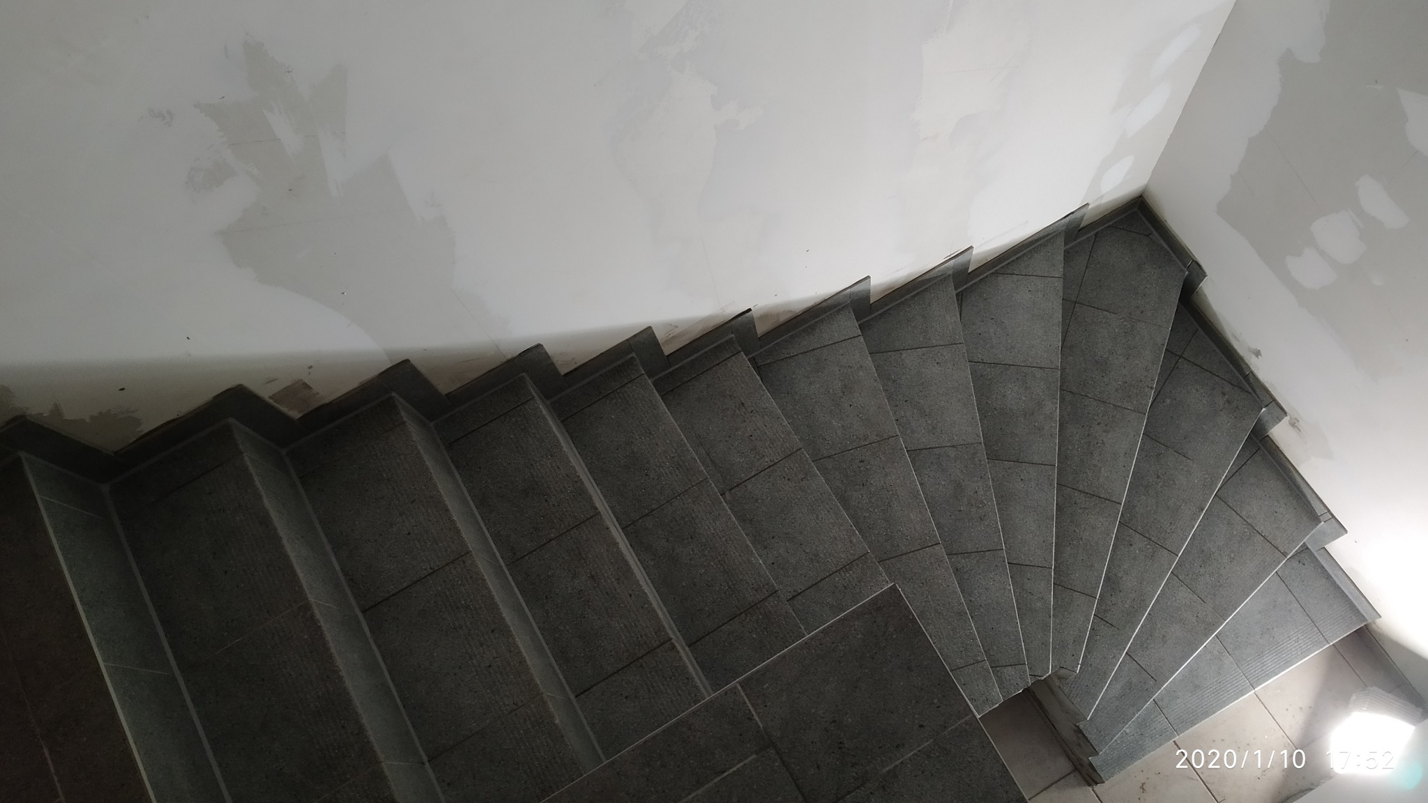 Wewnętrzne schody wyłożone szarymi płytkami ceramicznymi, widok z góry, ściany w trakcie przygotowania pod malowanie, z widocznymi śladami po szpachlowaniu.