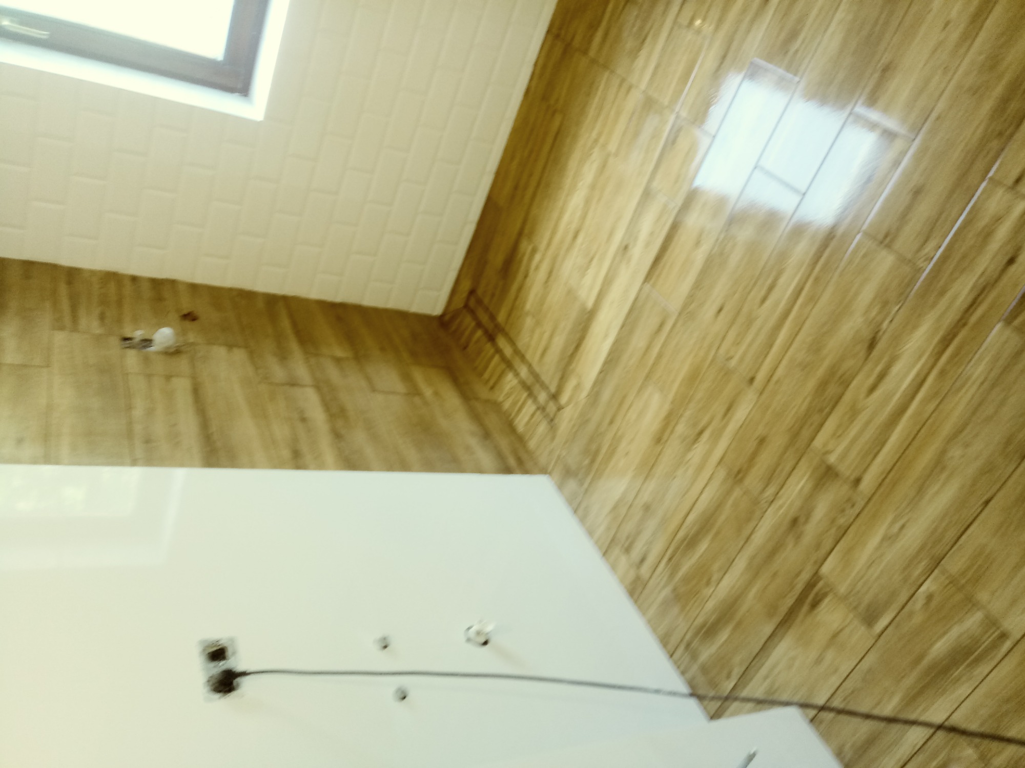 Wykończona łazienka z drewnopodobną podłogą i białymi płytkami na ścianie, widoczne gniazdka elektryczne przed montażem osprzętu.