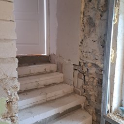 Rem-Bar - Murowane schody z białych bloczków w trakcie budowy, widoczne surowe ściany z instalacjami i pianką montażową, metalowy profil przy oknie.