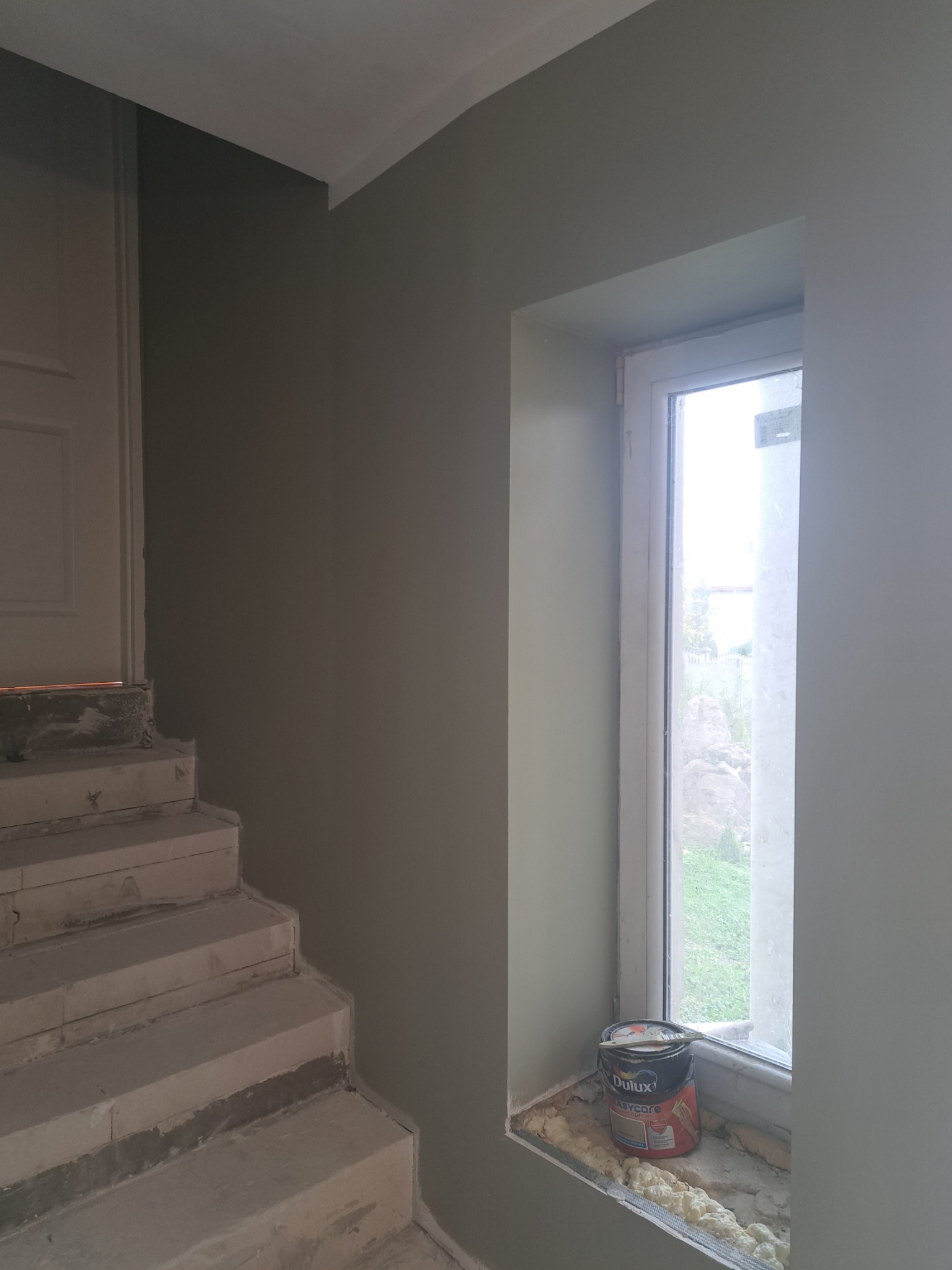 Świeżo pomalowane na oliwkowo ściany w Będzinie, widoczne schody w surowym stanie i puszka farby Dulux na parapecie okna.