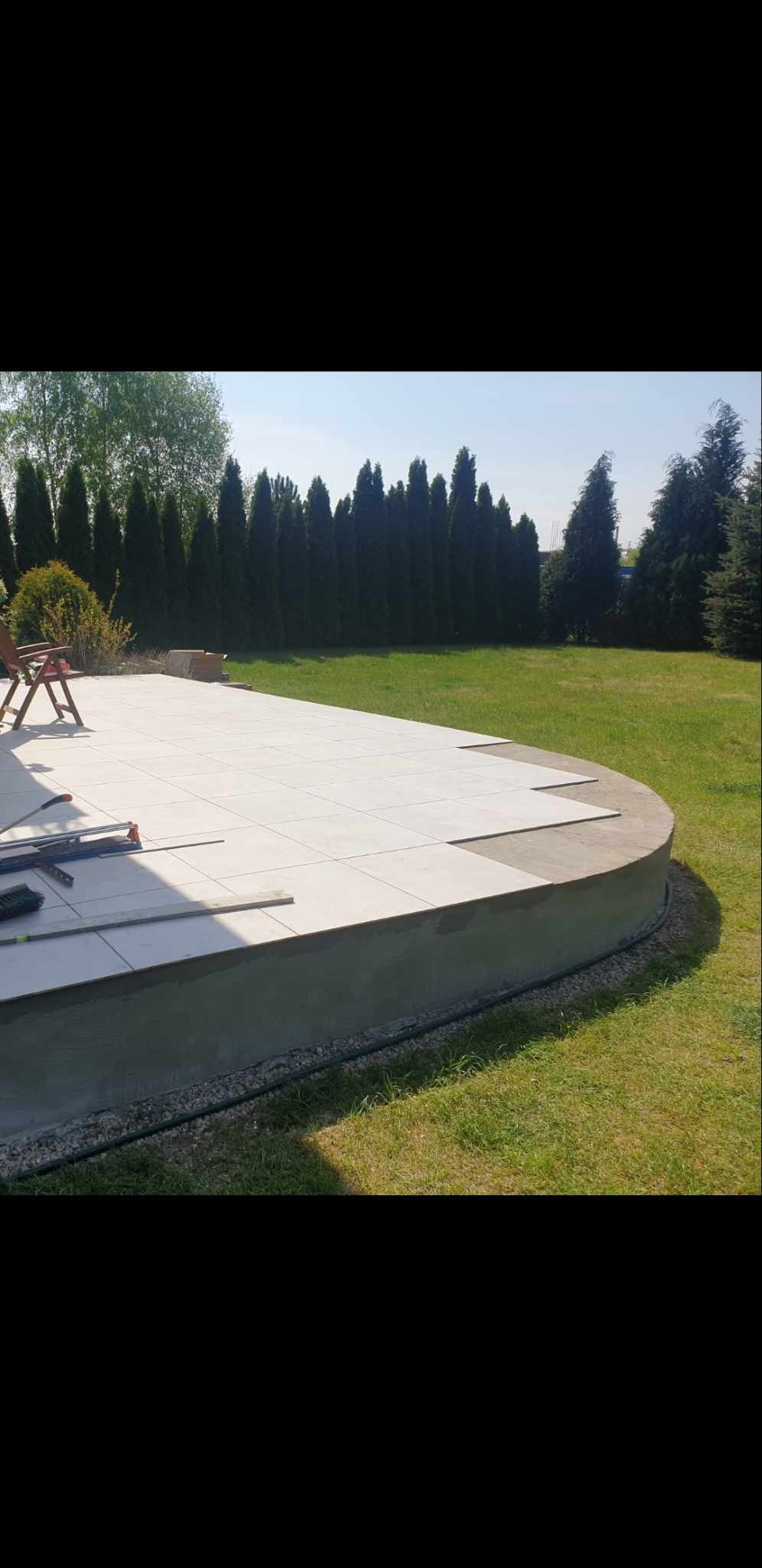 Układanie jasnych płytek na okrągłym tarasie w ogrodzie, widoczne narzędzia glazurnicze i częściowo ułożona powierzchnia.