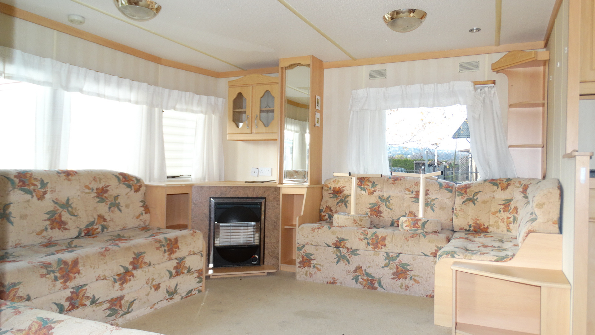 Jasne wnętrze domku holenderskiego z meblami w kwiaty, widok na kominek i okno z białymi firankami.