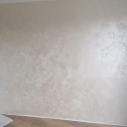 DH Daniel Haberski - Ściana z dekoracyjną, beżową fakturą imitującą marmur, widoczne gniazdka elektryczne i fragment podłogi laminowanej