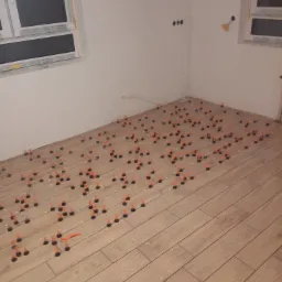 Układanie płytek podłogowych imitujących drewno, z użyciem systemu poziomowania płytek w narożniku pomieszczenia z oknami.