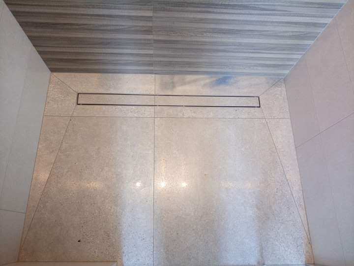 Wykończona kabina prysznicowa z odpływem liniowym, jasna płytka podłogowa i imitacja drewna na suficie, widok z góry.