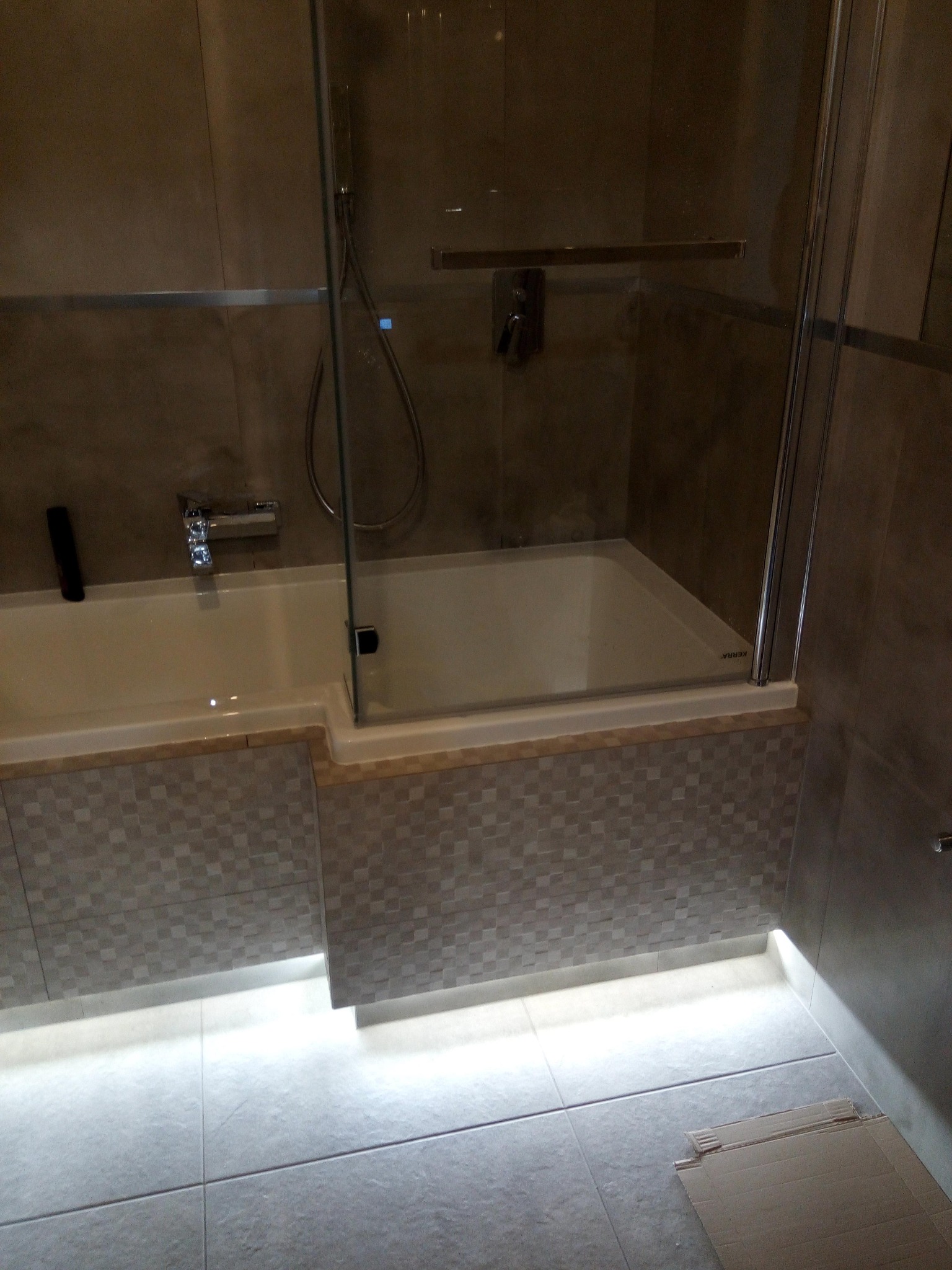 Nowoczesna łazienka z wanną obudowaną mozaiką i podświetleniem LED pod wanną, kabina prysznicowa ze szklanymi drzwiami.