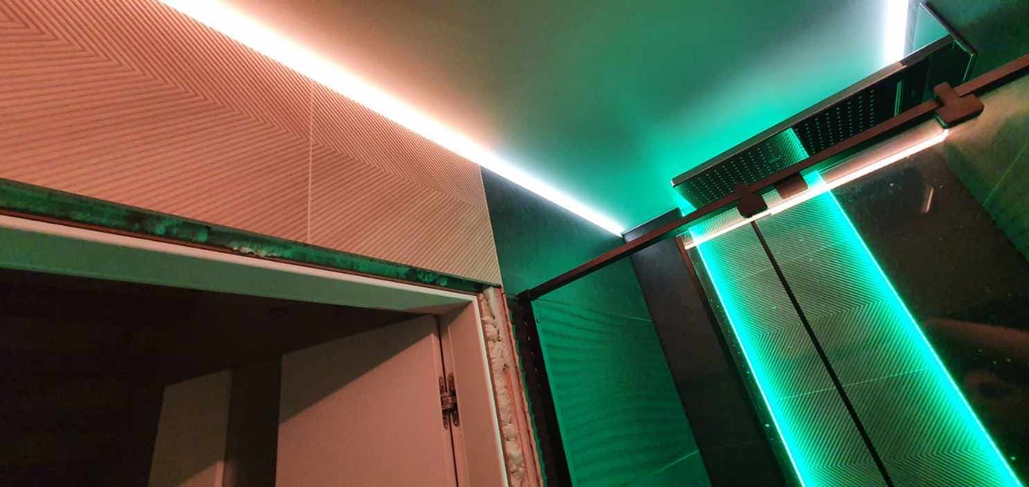 Nowoczesna kabina prysznicowa z zielonym podświetleniem LED i wzorzystymi panelami ściennymi, widoczna rama drzwi z pianką montażową.