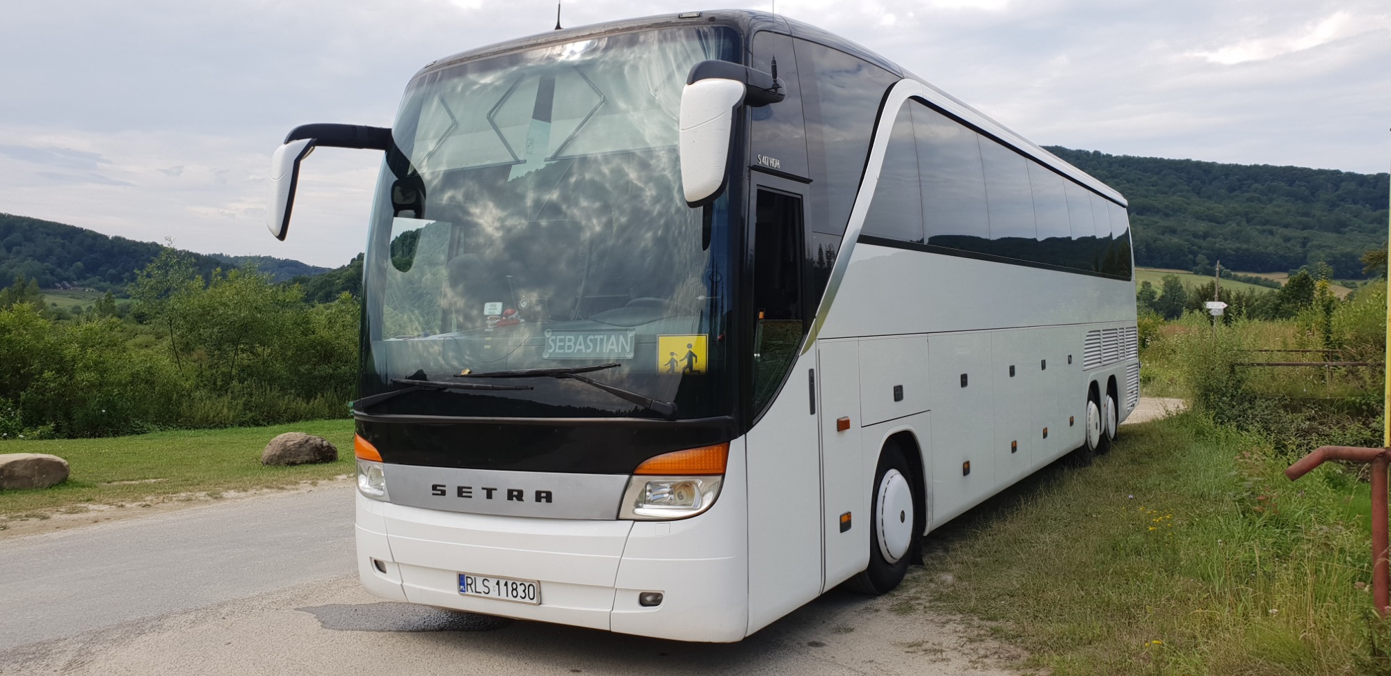 Biały autokar Setra S40 HDA z widoczną tablicą rejestracyjną RLS 11830, zaparkowany na tle zielonego krajobrazu.