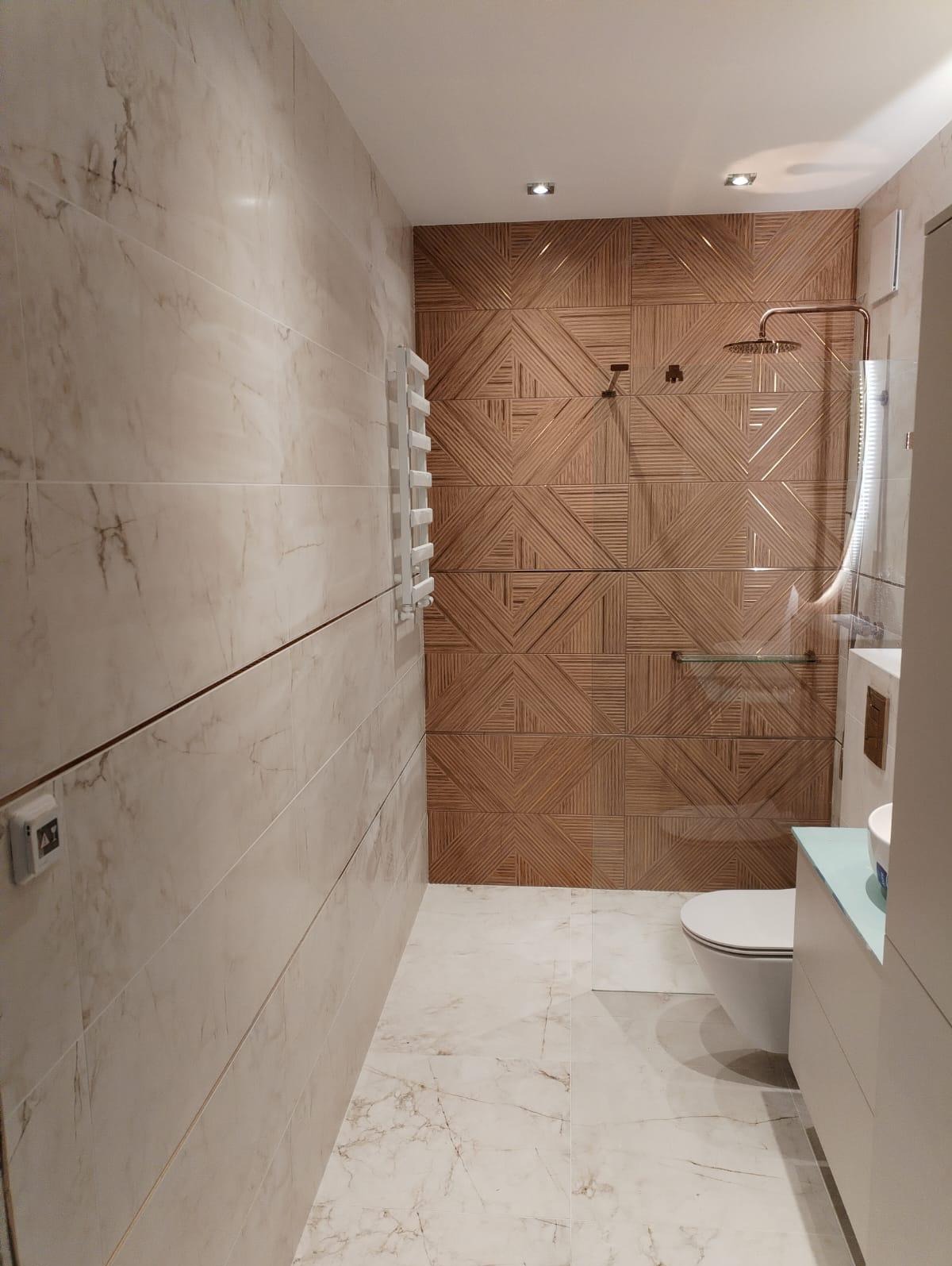 Nowoczesna łazienka z beżowymi płytkami imitującymi drewno na ścianie prysznicowej, marmurowe płytki na podłodze i ścianach, oraz białą armaturą.