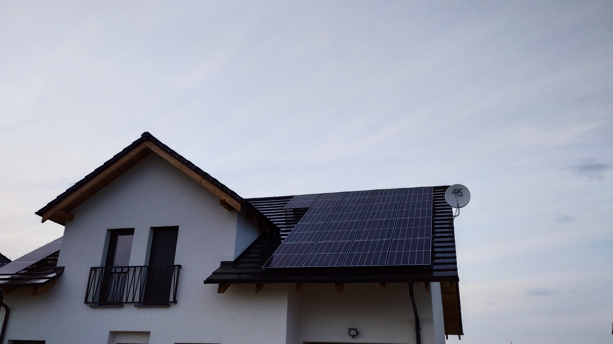 Biały dom jednorodzinny z zamontowanymi panelami fotowoltaicznymi na dachu i anteną satelitarną.