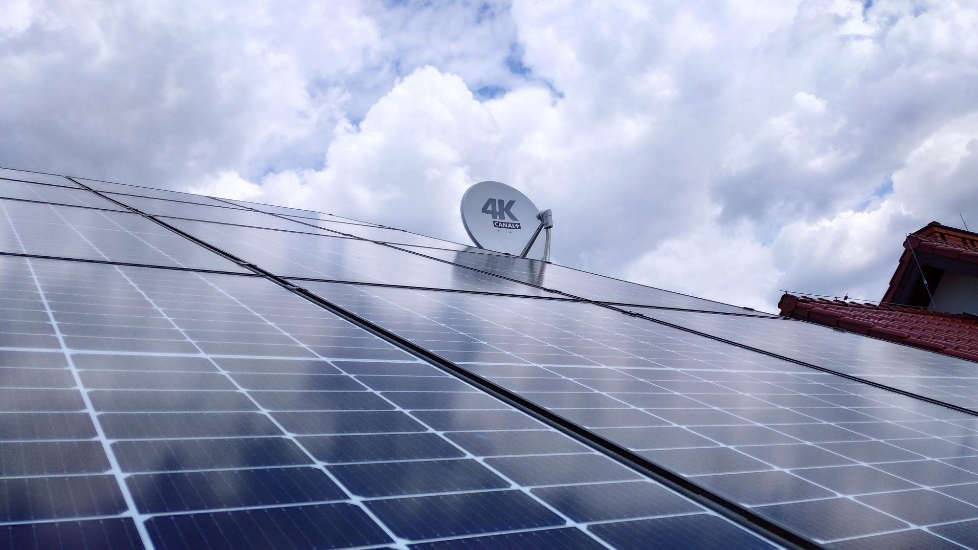Panele słoneczne na dachu domu pod pochmurnym niebem, z widoczną anteną satelitarną 4K Canal+ pośród paneli.